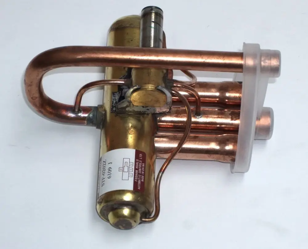 Daikin 4-Wege-Ventilkörper aus Kupfer mit mehreren Rohren und einem goldfarbenen Element. Sichtbarer Aufkleber mit Modellnummer und Seriennummer.